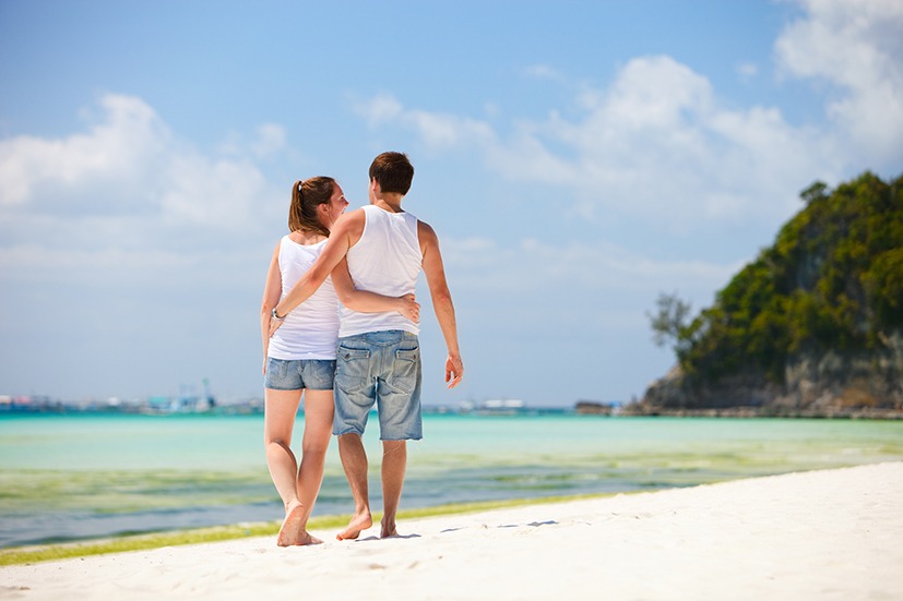 Back view of young romantic couple walking along tropical beach