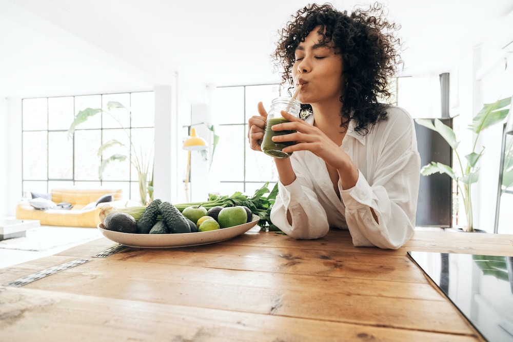 woman drinking green juice in kitchen