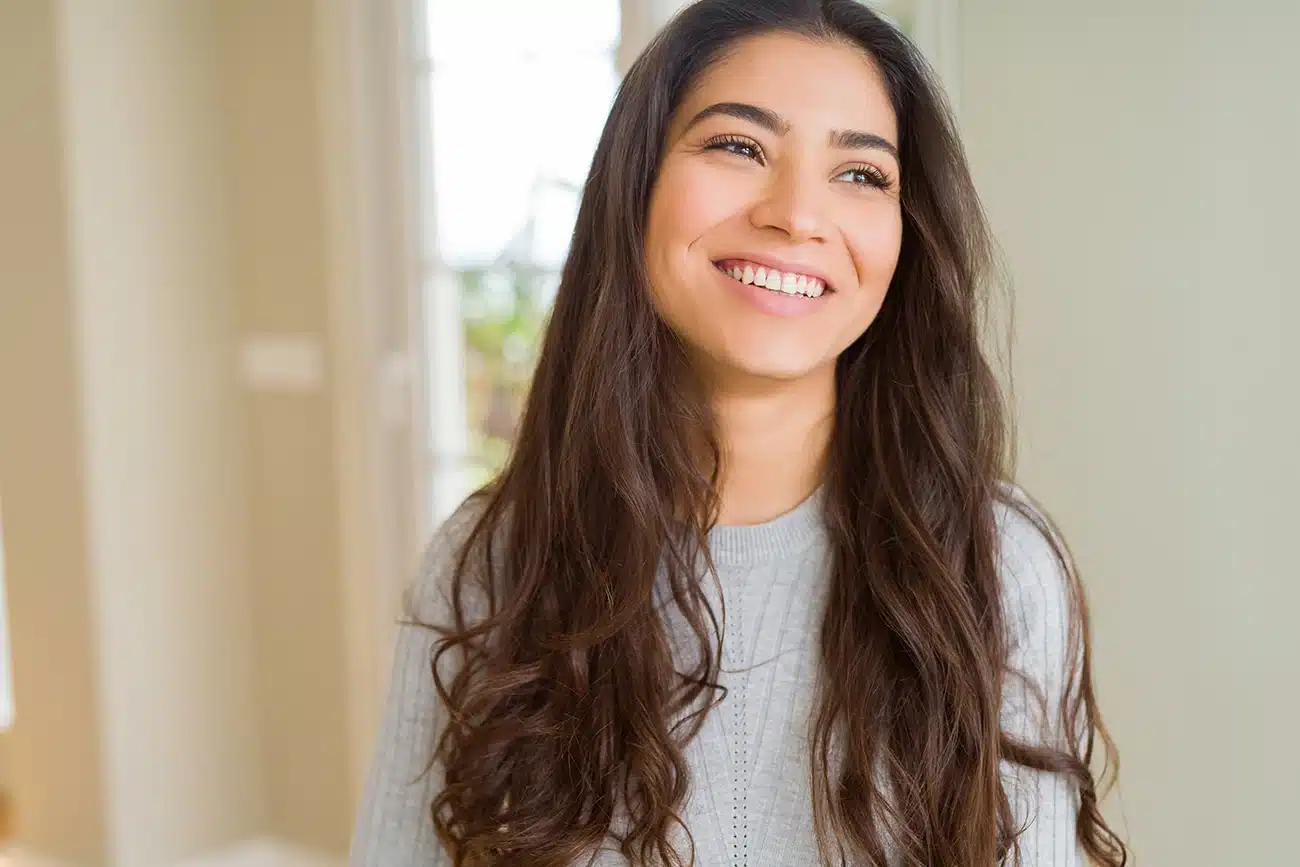 Smiling young brunette woman with long wavy hair looking up in a brightly lit room. Smiling young brunette woman with long wavy hair looking up in a brightly lit room.