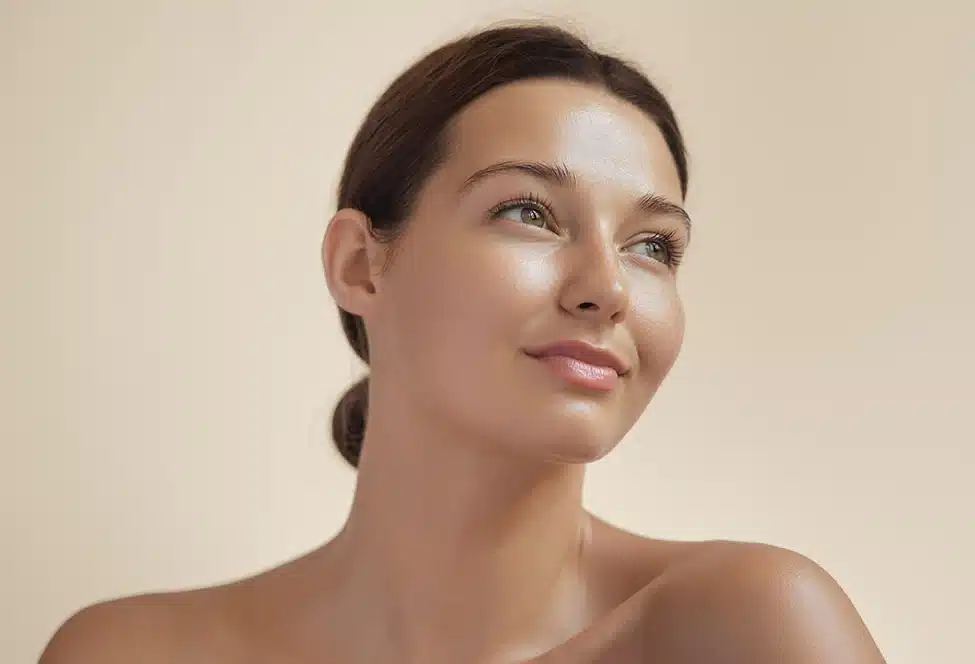 Woman with radiant skin looking up and smiling against a beige background.